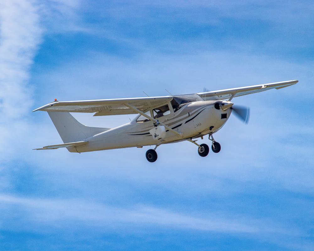 A white Cessna airplane flying amid a bright, blue sky.