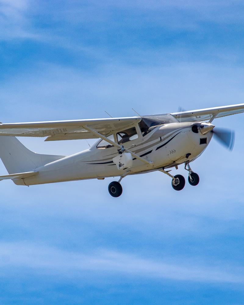 A white Cessna airplane flying amid a bright, blue sky.