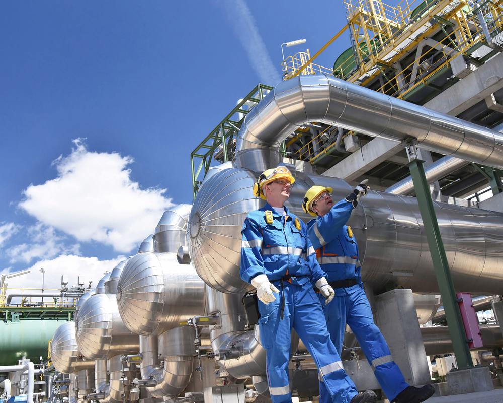 Two workers in hard hats and reflective work attire walking through a natural gas processing facility