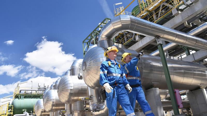 Two workers in hard hats and reflective work attire walking through a natural gas processing facility