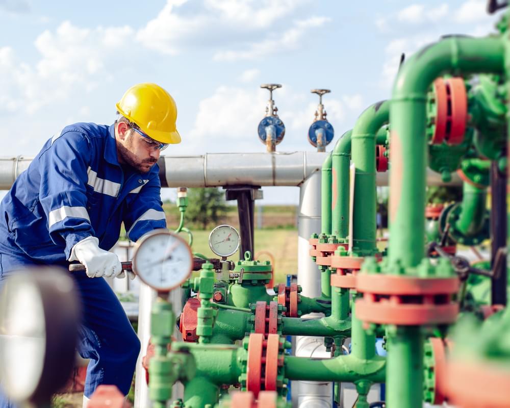 Man in a hard hat and reflective jacket using a wrench on a pipeline valve