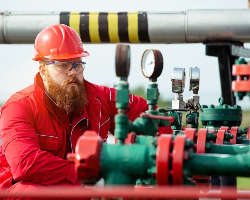 A man in a hard hat inspects pipeline valves