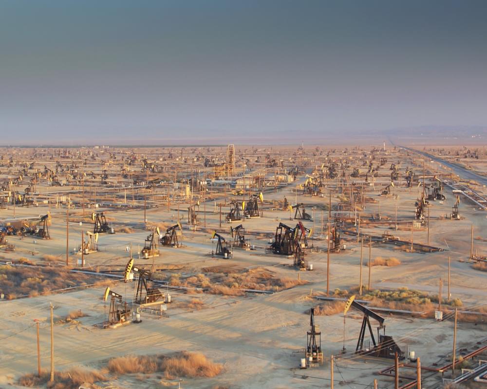 Wide view of a desert oil field with dozens of oil well heads and pump jacks