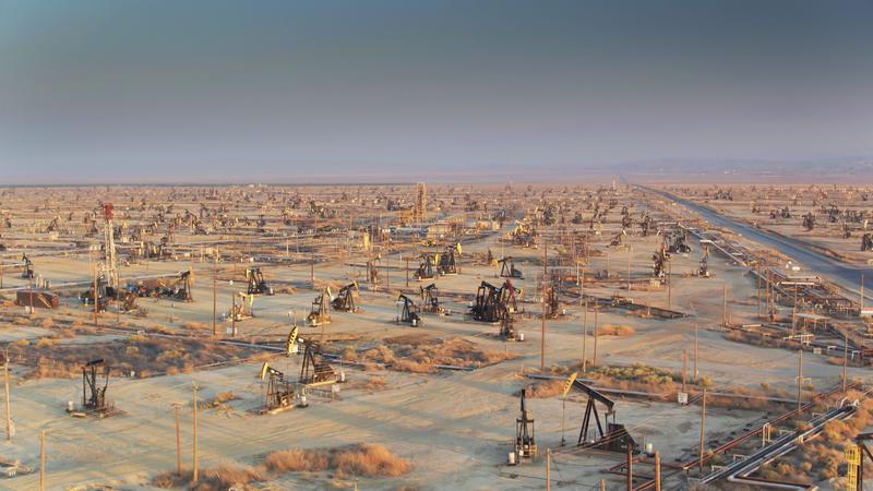 Wide view of a desert oil field with dozens of oil well heads and pump jacks