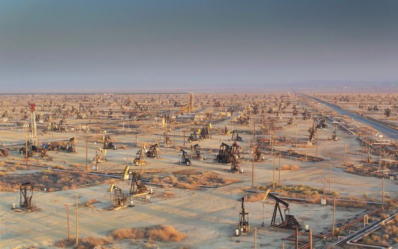 Wide view of a desert oil field with dozens of oil well heads and pump jacks