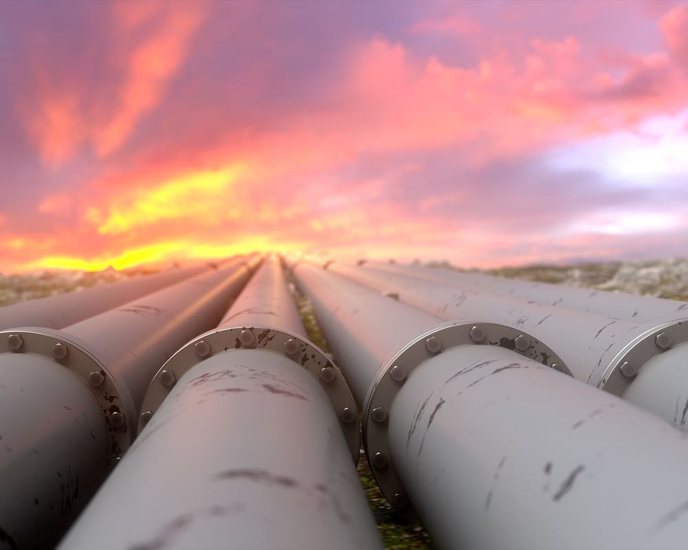 Close up of four over ground pipelines that extend into the distance while the sun rises