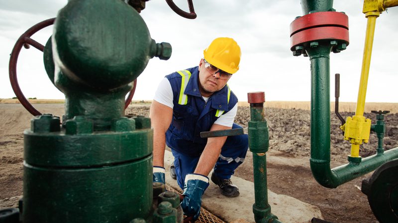 Man in a hardhat and safety vest working on a pipeline valve
