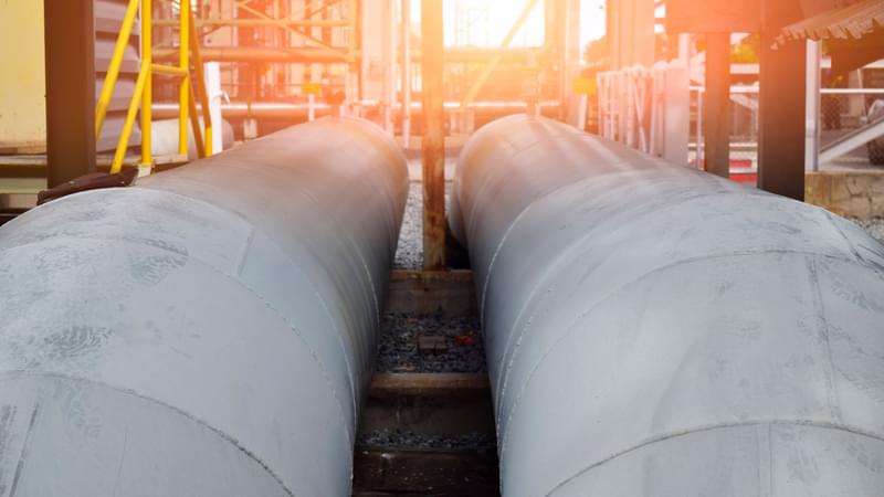 Two pipelines heading towards some scaffolding with a warm glowing light emanating from the background